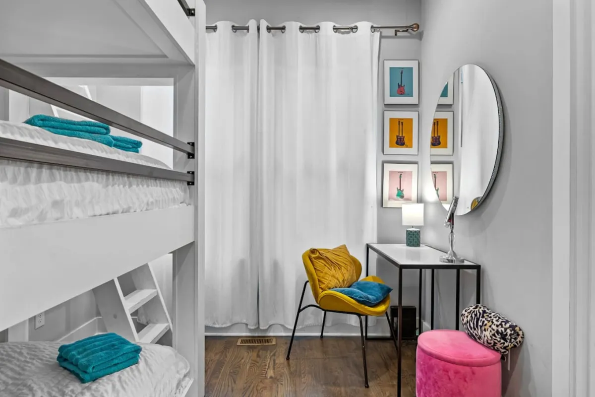 A cozy bedroom highlights custom bunk beds and a colorful chair set beside a playful round mirror and vibrant wall artwork. The thoughtful arrangement encourages late-night chats, reading, and creative inspiration, ideal for accommodating multiple guests.