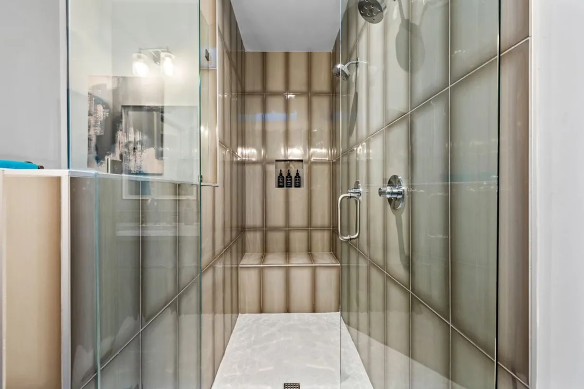 A modern bathroom featuring a sleek glass shower enclosure, textured tiles, and updated fixtures. The serene atmosphere is designed for relaxing showers and unwinding after a busy day.