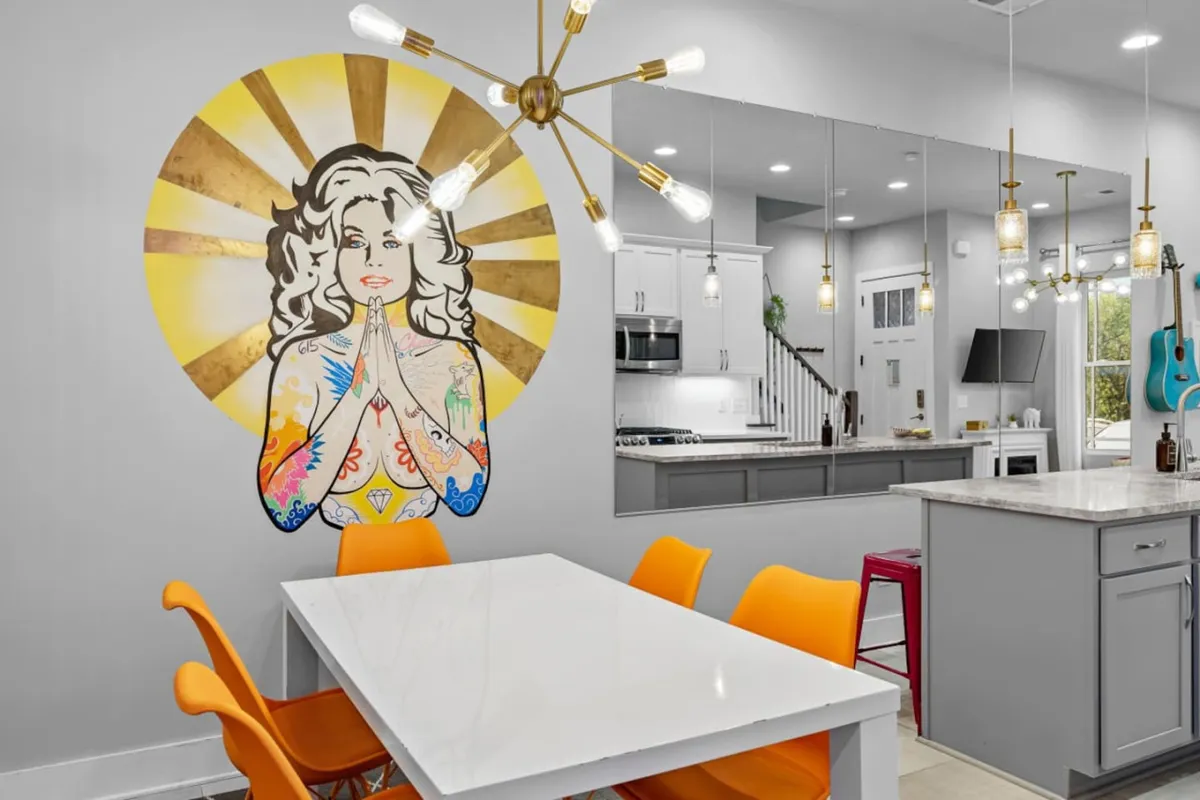 A vibrant dining area featuring a colorful mural, modern lighting, bright orange chairs, and a sleek dining table. The space is ideal for creative gatherings and social meals, showcasing a playful atmosphere.