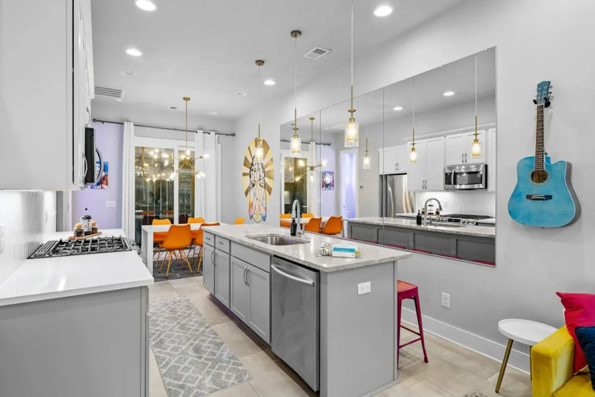 A spacious, cheerful kitchen and dining area with a kitchen island, colorful chairs, a wall-mounted guitar, and expressive artwork. The setting is perfect for group cooking sessions, family-style meals, and musical evenings with friends.