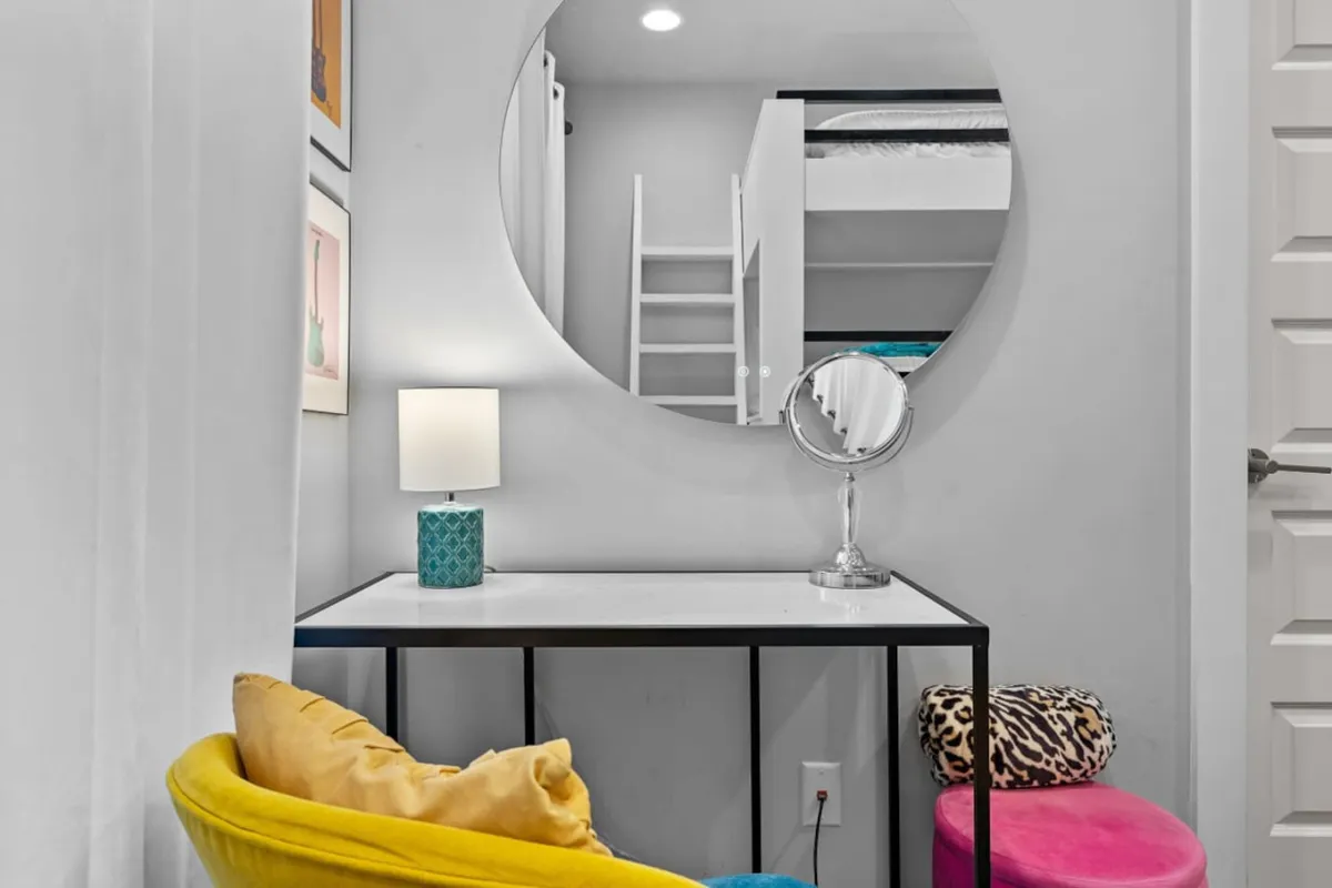 A cheerful nook with a round mirror, colorful chairs, and a desk with a lamp, perfect for getting ready or enjoying a quiet moment. The space feels bright and inviting, ideal for pre-night-out glam or catching up with friends.