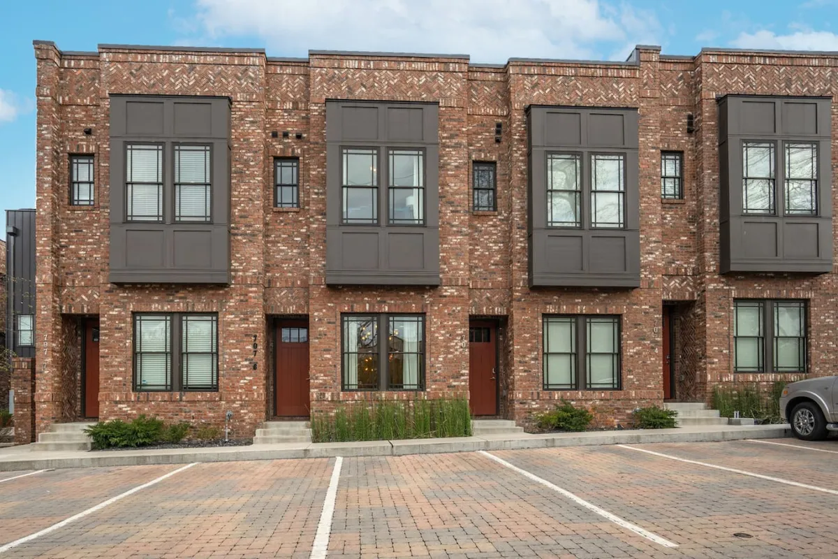 This exterior image captures the brick facade of the property with large windows and decorative trim. The porch area is visible, inviting residents to enjoy coffee or socialize outdoors while being partially shielded from the street. The overall mood is welcoming, with potential for gathering or quiet moments.