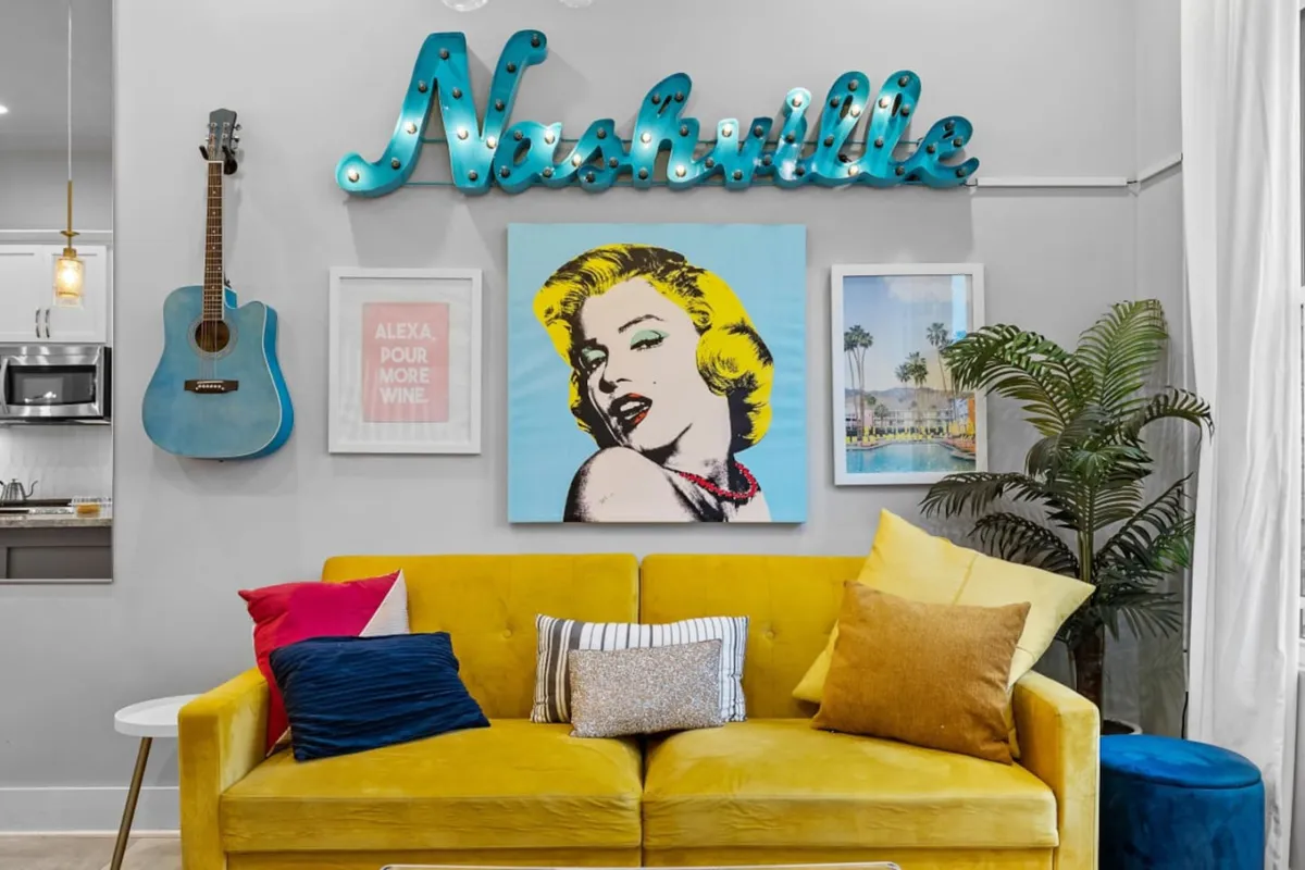A lively living area featuring a bold Nashville sign, a striking blue guitar, Marilyn Monroe artwork, a yellow sofa adorned with decorative cushions, and tasteful artistic decor. The space radiates a vibrant, urban energy—perfect for relaxing or entertaining guests.